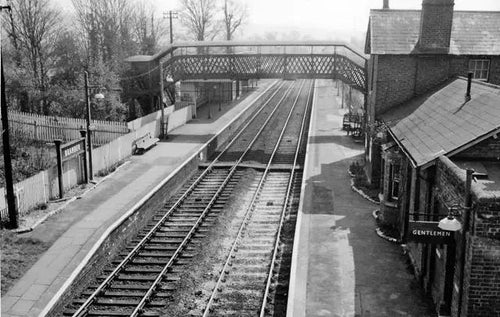 Vintage black and white photograph of a railway station with tracks and buildings.