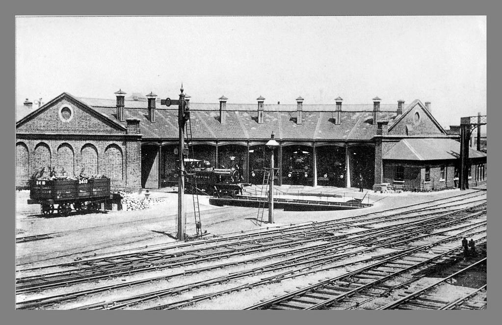 Vintage black and white photograph of a train station with tracks and buildings.