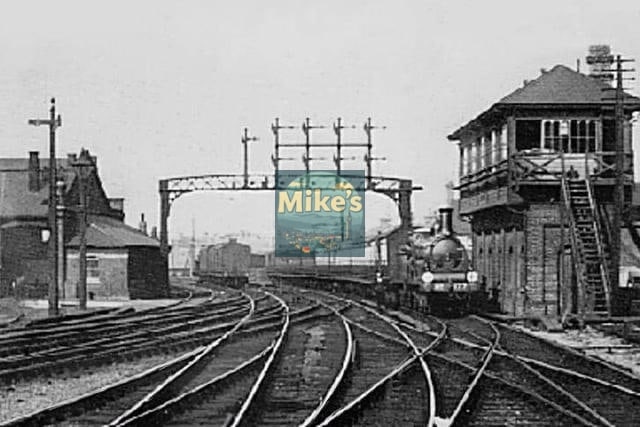 Vintage black and white photograph of a train station with tracks and a signal tower.