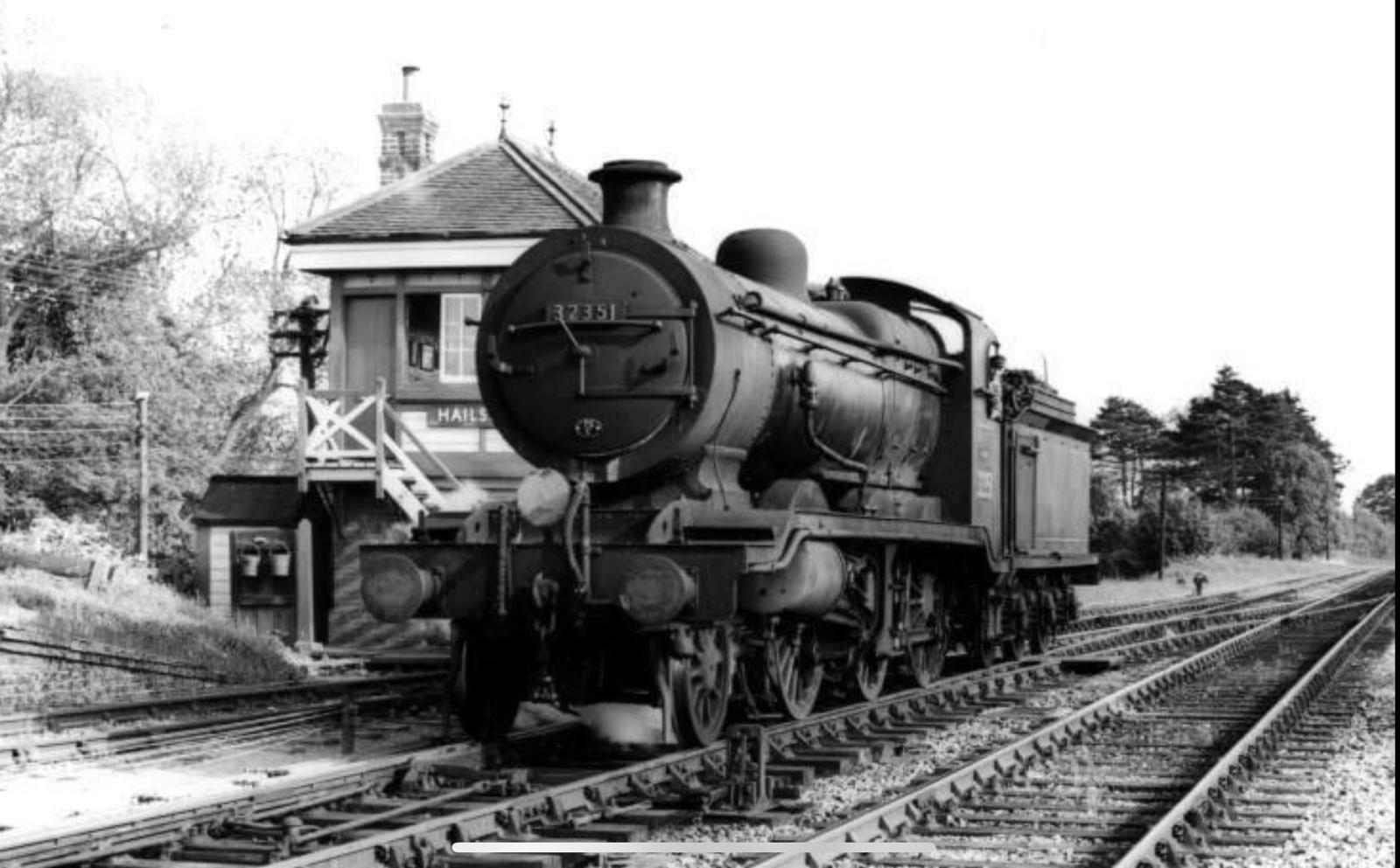 Vintage steam locomotive on railway tracks with a signal box in the background