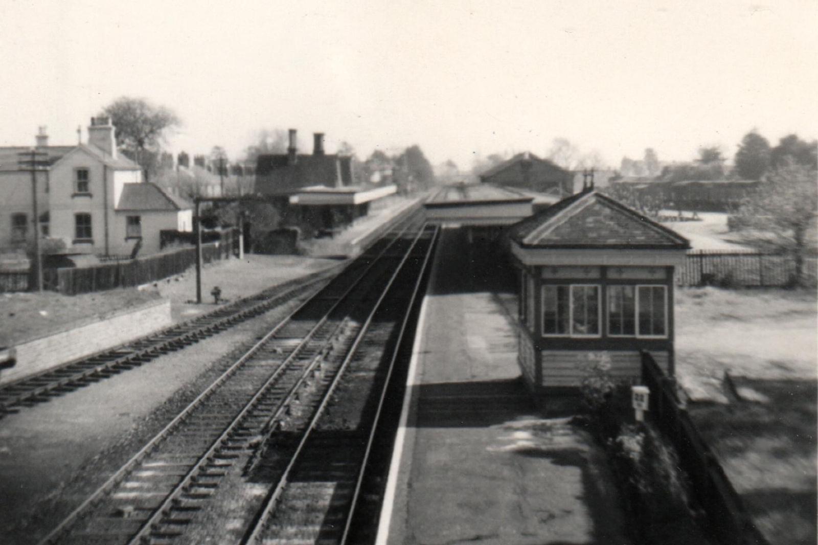 Vintage black and white photograph of a railway station with tracks and buildings.