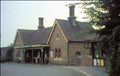 Old brick building with a roof overhang and two chimneys, surrounded by trees.