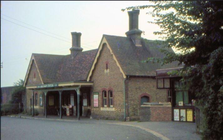 Old brick building with a roof overhang and two chimneys, surrounded by trees.