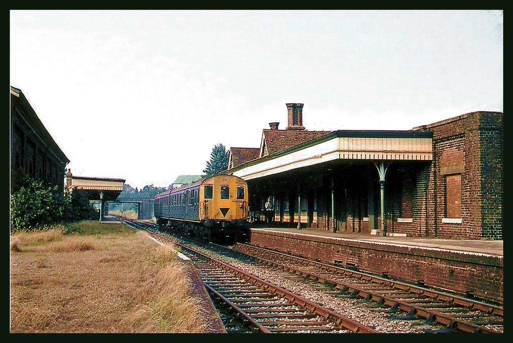 Vintage train at a station with a brick building and overhanging roof.