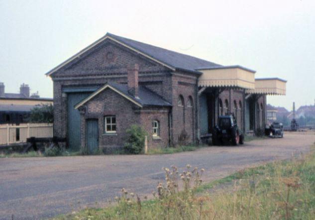 Old brick building with a car parked in front, surrounded by grass and a clear sky.
