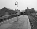 Vintage black and white photograph of a train station with a train on the tracks and buildings in the background.