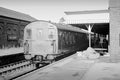 Vintage train at a station platform with brick building and overpass in the background