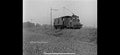 Vintage black and white photograph of a small locomotive on a dirt track with power lines in the background.