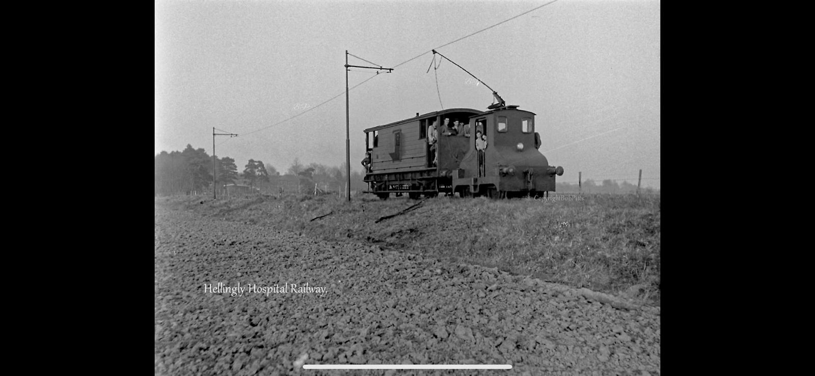 Vintage black and white photograph of a small locomotive on a dirt track with power lines in the background.