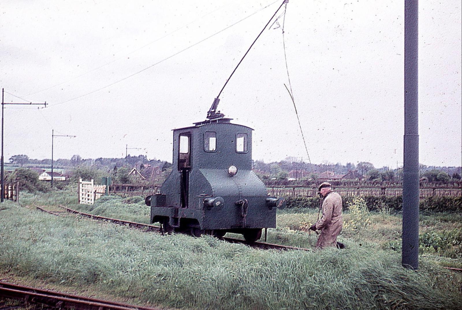 Small railway engine on tracks with a person nearby, set against a rural landscape.