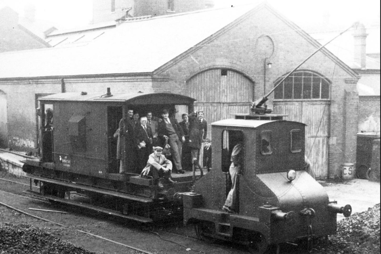 Vintage steam locomotive with people around it in front of a building.