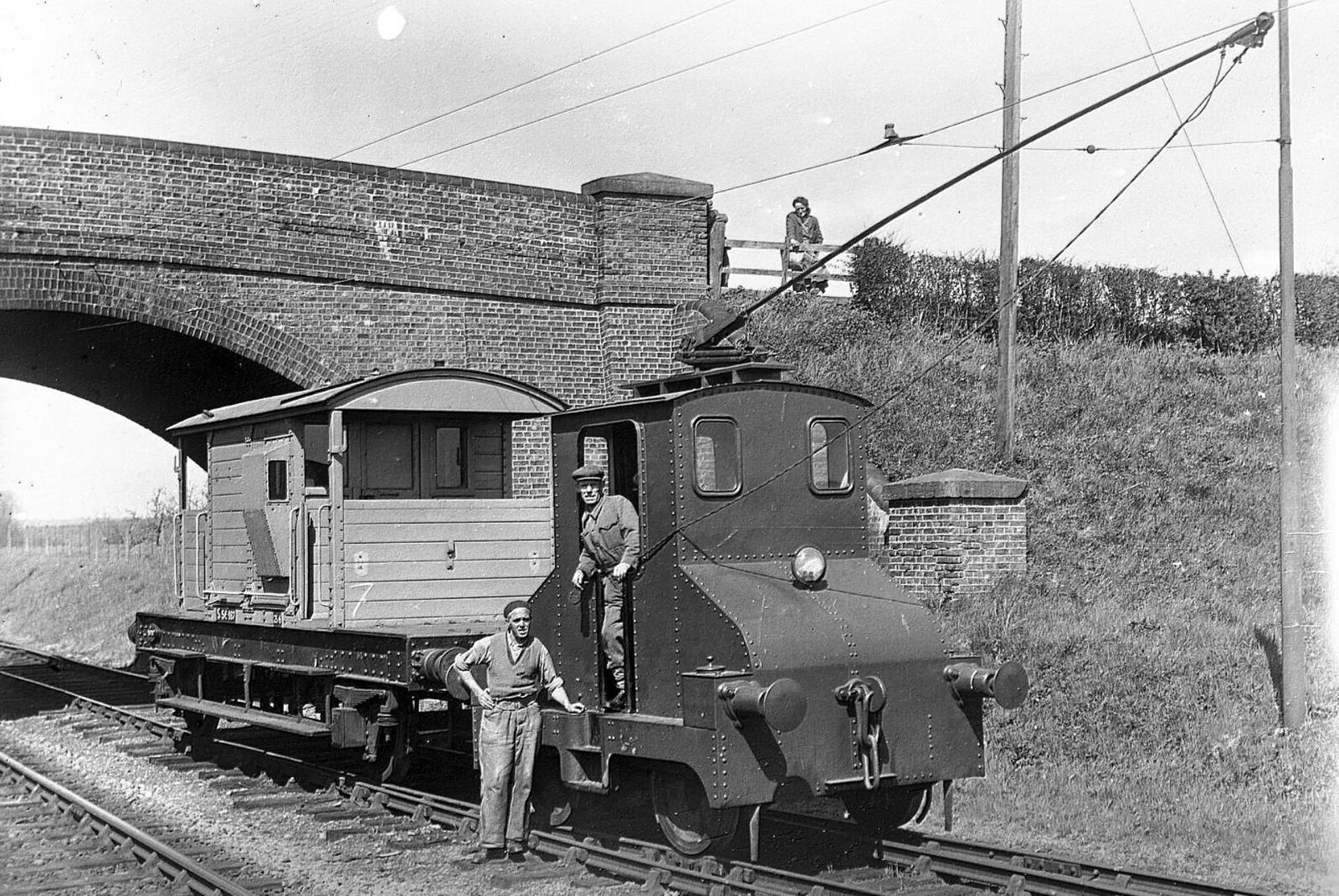 Vintage black and white photograph of a small train on tracks with people around.