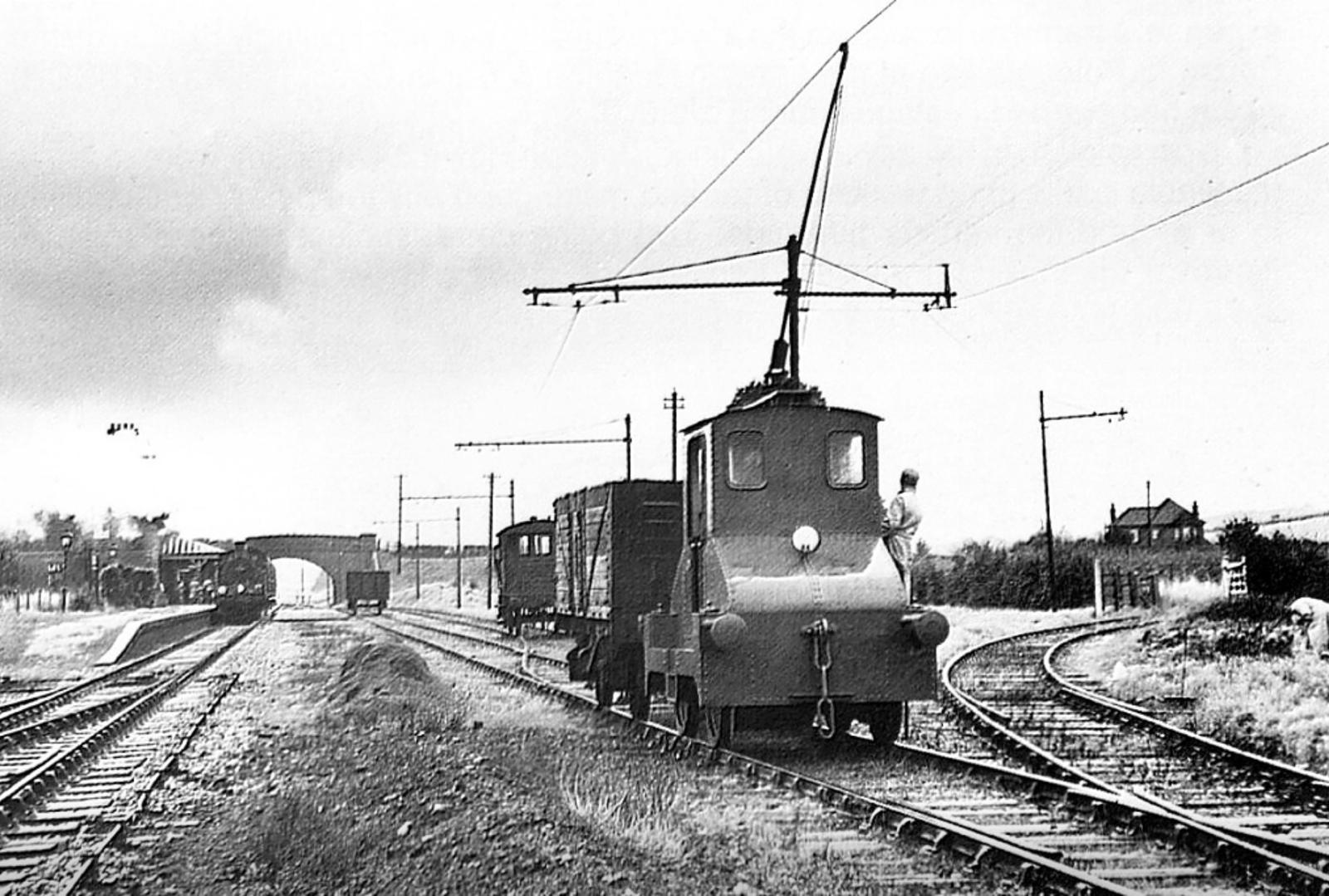 Vintage black and white photograph of a train on tracks with overhead electric lines.