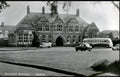 Historic black and white photo of a large building with cars and a bus in front