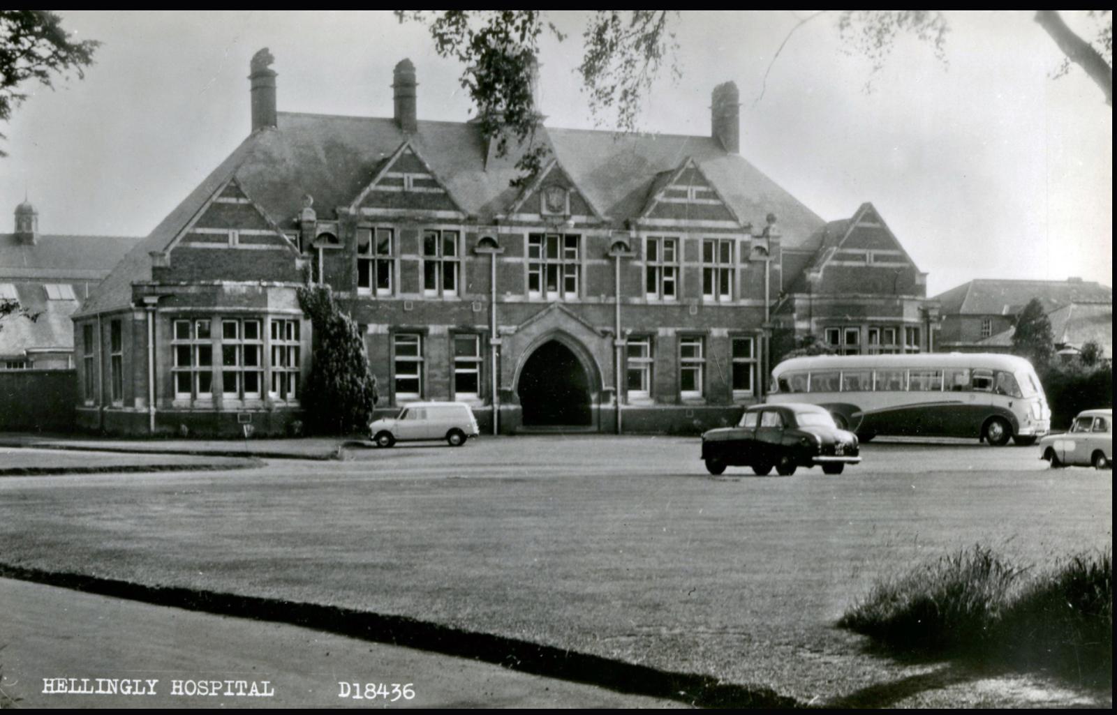 Historic black and white photo of a large building with cars and a bus in front