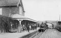 Vintage black and white photograph of a train station with a steam locomotive and platform.