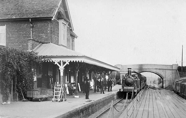 Vintage black and white photograph of a train station with a steam locomotive and platform.