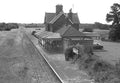Vintage black and white photograph of a rural train station with a platform and building.