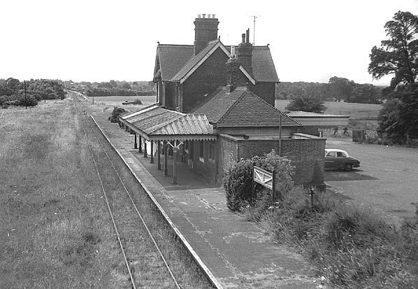 Vintage black and white photograph of a rural train station with a platform and building.