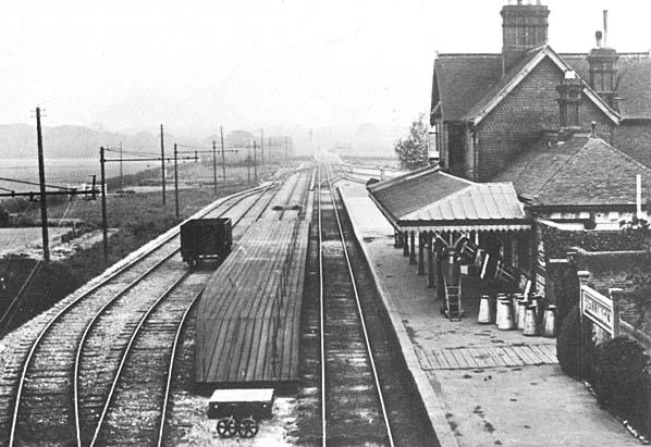 Vintage black and white photograph of a train station with tracks and buildings.