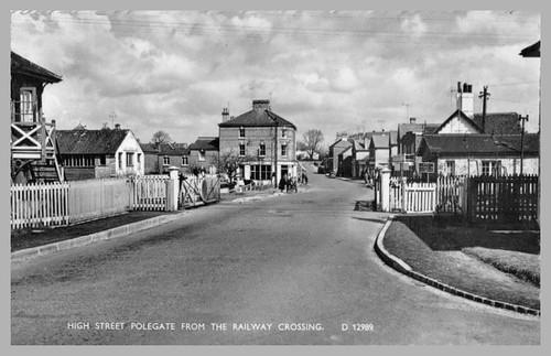 Vintage black and white photo of a town street with buildings and people from a railway crossing perspective.