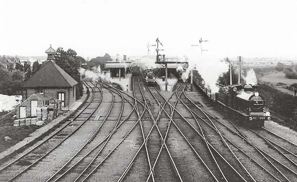 Vintage black and white photograph of a train station with a steam train on tracks.