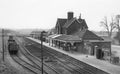 Vintage black and white photograph of a train station with a station building and tracks.