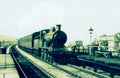 Vintage steam train on tracks with a platform and building in the background
