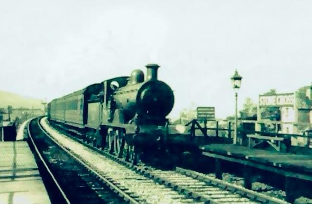 Vintage steam train on tracks with a platform and building in the background