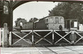 Vintage black and white photograph of a train crossing a level crossing with a person standing nearby.